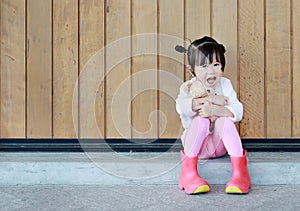 Portrait of cute little girl sit and hugging Teddy Bear against wood plank wall