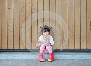 Portrait of cute little girl sit and hugging Teddy Bear against wood plank wall