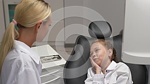 Portrait of cute little girl sitting on dental chair and complaining about pain visiting pediatric dentist. Prevention