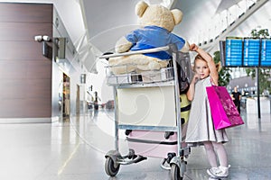 Portrait of cute little girl standing next to baggage cart in airport