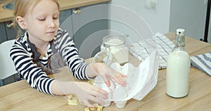 Portrait of a cute little girl taking eggs from a package helping mom cooking homemade cookies together in the kitchen