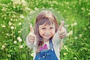 Portrait of cute little girl with thumbs up shows a class on the flower meadow, happy childhood concept, child having fun photo