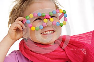 Portrait of cute little girl wearing funny glasses, decorated with colorful smarties, candies