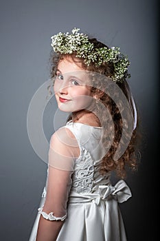 Portrait of cute little girl on white dress and wreath of first holy communion. First Communion Day. Studio photo