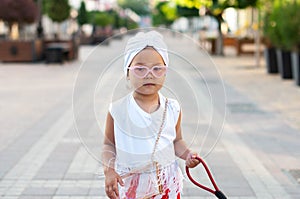 Portrait of a cute little girl with a white turban on her head, pink heart-shaped glasses