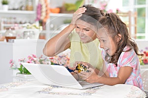 Portrait of cute little girl with young mother playing computer game with laptop
