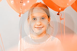 Portrait of a cute little happy candid smiling caucasian eight year old kid girl with red balloons against the background of a gra