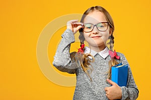 Portrait of a cute little kid girl on a yellow background. Child schoolgirl looking at the camera, holding a book.