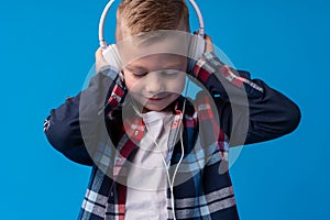 Portrait of a cute little kid in headphones listening to music over blue background