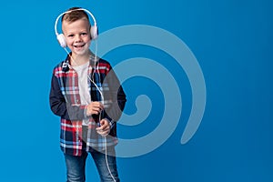 Portrait of a cute little kid in headphones listening to music over blue background