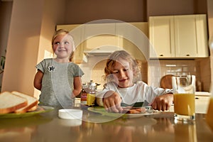 Portrait of cute little kids preparing lunch or breakfast for themselves. Cheerful boy spreading chocolate nut butter on