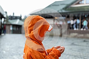Portrait cute little lonely caucasian kid boy in bright orange waterproof raincoat stand under rain and enjoy catching