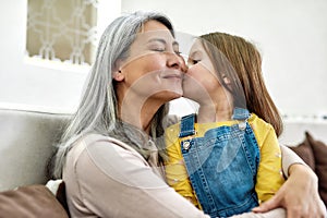 Portrait of cute little preschool granddaughter kissing her grandmother while spending time together at home