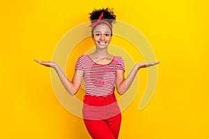 Portrait of cute little schoolgirl arms palms hold demonstrate empty space vs scales isolated on yellow color background