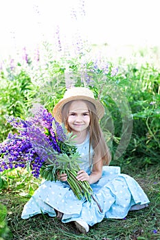 Portrait of a cute little smiling brunette girl with long beautiful hair in a straw hat, against the background of a flowering mea