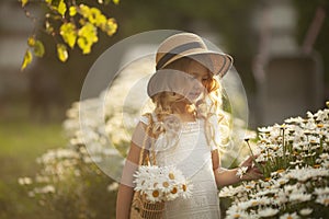 Portrait of a cute little smiling girl in a straw hat with a basket of flowers in a chamomile field in spring.