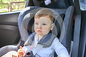 Portrait of cute little thoughtful baby sitting in the baby car seat looking forward.