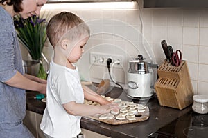 Portrait cute little toodler caucasian boy kid cooking sweet tasty cookies with young adult mother at home kitchen. Mom