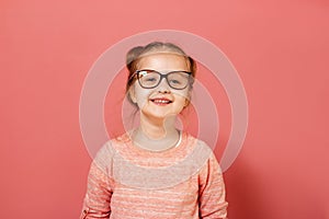 Portrait of a cute little 6 year old girl wearing eyeglasses on a pink background