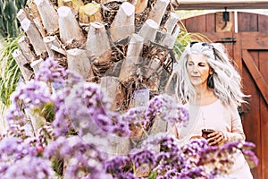 Portrait of cute mature caucasian woman with long white hair trendy drinking a naturel tea in a garden outside home - diversity