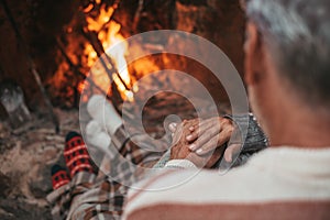 Portrait of cute mature senior enjoying Christmas in front of hot fireplace at home feeling cold embracing together and holding