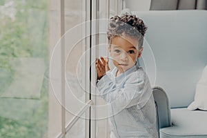 Portrait of cute mixed race curly haired baby boy waiting for parents near window