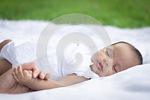 Portrait of cute new born baby girl is lie and holding her mother `s hand on the white cloth mattress in the lawn