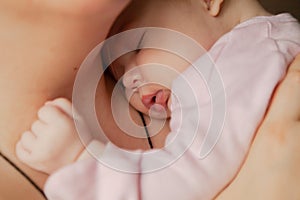 Portrait of a cute newborn baby girl sleeping on her mother`s shoulder at home