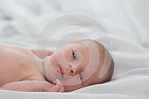 Portrait of a cute newborn baby looking into the camera. Little boy 7 days, one week. The baby lies on a white silk blanket.