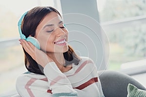 Portrait of cute positive girl toothy smile closed eyes hand touch headphones free time relax apartment inside