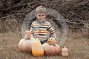 Portrait of cute preschool boy sitting in field near big pumpkins decorated for Halloween. child grimaces, frightens. October,