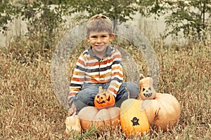 Portrait of cute preschool boy sitting in field near big pumpkins decorated for Halloween. October, outdoor. Harvesting