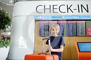 Portrait of cute preteen boy in international airport or on railway station platform near information display of timetable. Check-