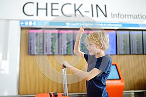 Portrait of cute preteen boy in international airport or on railway station platform near information display of timetable. Check-