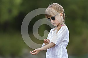 Portrait of cute pretty funny young girl with blond braids in white dress and dark sunglasses.