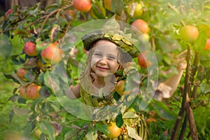 Portrait of a cute pretty girl in a green gnome hat in a tree with apples.