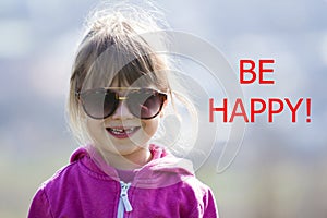 Portrait of cute pretty little blond preschool girl in pink sweater and dark sunglasses smiling happily in camera with funny