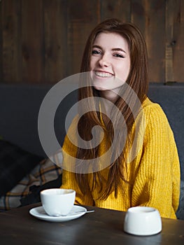 Portrait of a cute pretty redhead smiling woman sitting in a cafe enjoying free time coffee break with a cup of cappuccino