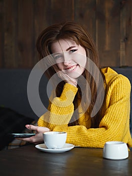 Portrait of a cute pretty redhead woman holding smartphone sitting in a cafe enjoying free time coffee break with a cup of