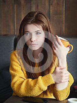 Portrait of a cute pretty redhead woman sitting in a cafe enjoying free time coffee break with a yellow mug in her hands.