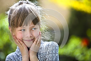 Portrait of cute pretty thoughtful child girl outdoors on blurred sunny colorful bright background