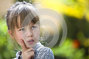 Portrait of cute pretty thoughtful child girl outdoors on blurred sunny colorful bright background