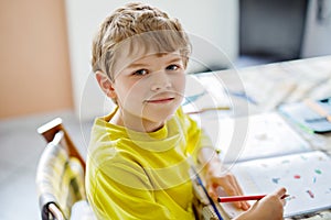 Portrait of cute school kid boy at home making homework. Little concentrated child writing with colorful pencils