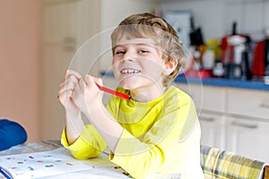 Portrait of cute school kid boy at home making homework. Little concentrated child writing with colorful pencils