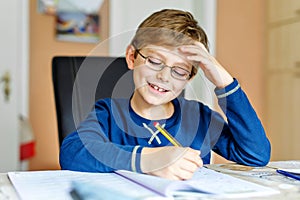 Portrait of cute school kid boy wearing glasses at home making homework. Little concentrated child writing with colorful