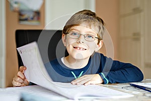 Portrait of cute school kid boy wearing glasses at home making homework. Little concentrated child writing with colorful