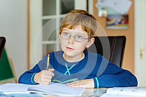 Portrait of cute school kid boy wearing glasses at home making homework. Little concentrated child writing with colorful