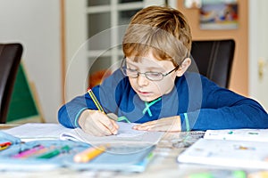 Portrait of cute school kid boy wearing glasses at home making homework. Little concentrated child writing with colorful