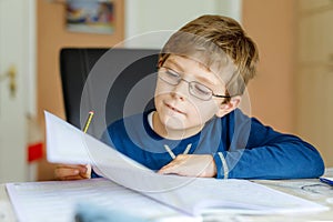 Portrait of cute school kid boy wearing glasses at home making homework. Little concentrated child writing with colorful