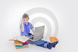 Portrait of cute schoolboy sitting with books and typing on laptop keyboard